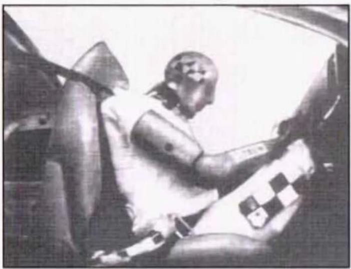 Black-and-white photo of a person seated in a car, wearing a checkered and cap (no visible text or symbols)