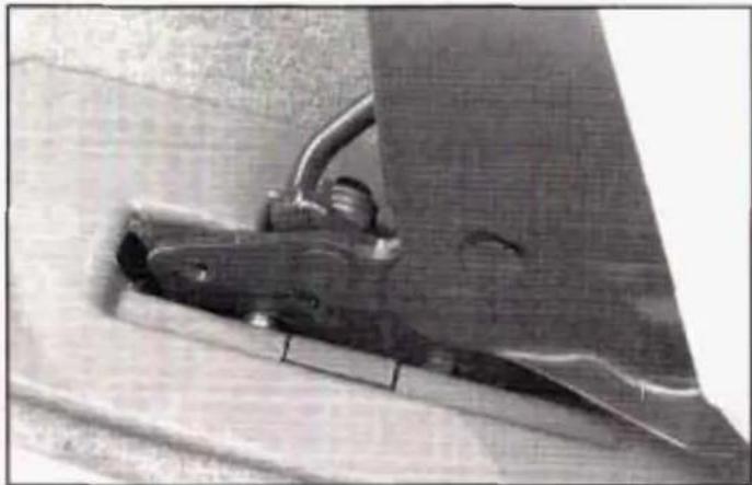 Close-up of a metallic mechanical component with a curved handle and angled blade, mounted on a surface (no visible text or symbols)