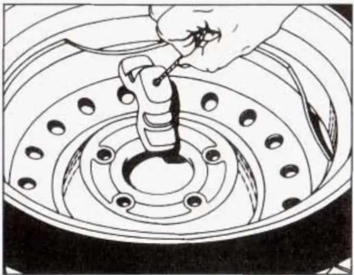 Illustration of a hand using a tool to adjust or install a car tire component (no text or symbols visible)