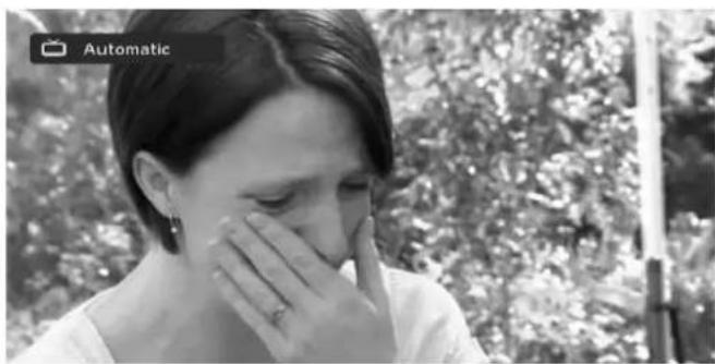 Black-and-white photo of a woman covering her face with hand near her mouth, outdoors with foliage background (no visible text or symbols)