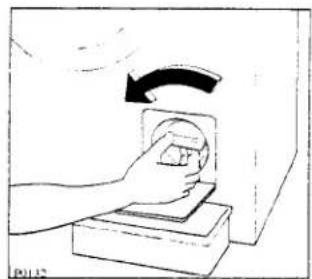 Hand pressing a circular object on a base, with an arrow indicating rotation (no text or symbols)