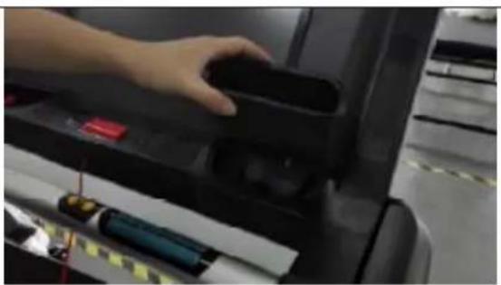 Close-up of a hand pressing down on a black electronic device with a red control panel and battery (no visible text or symbols)