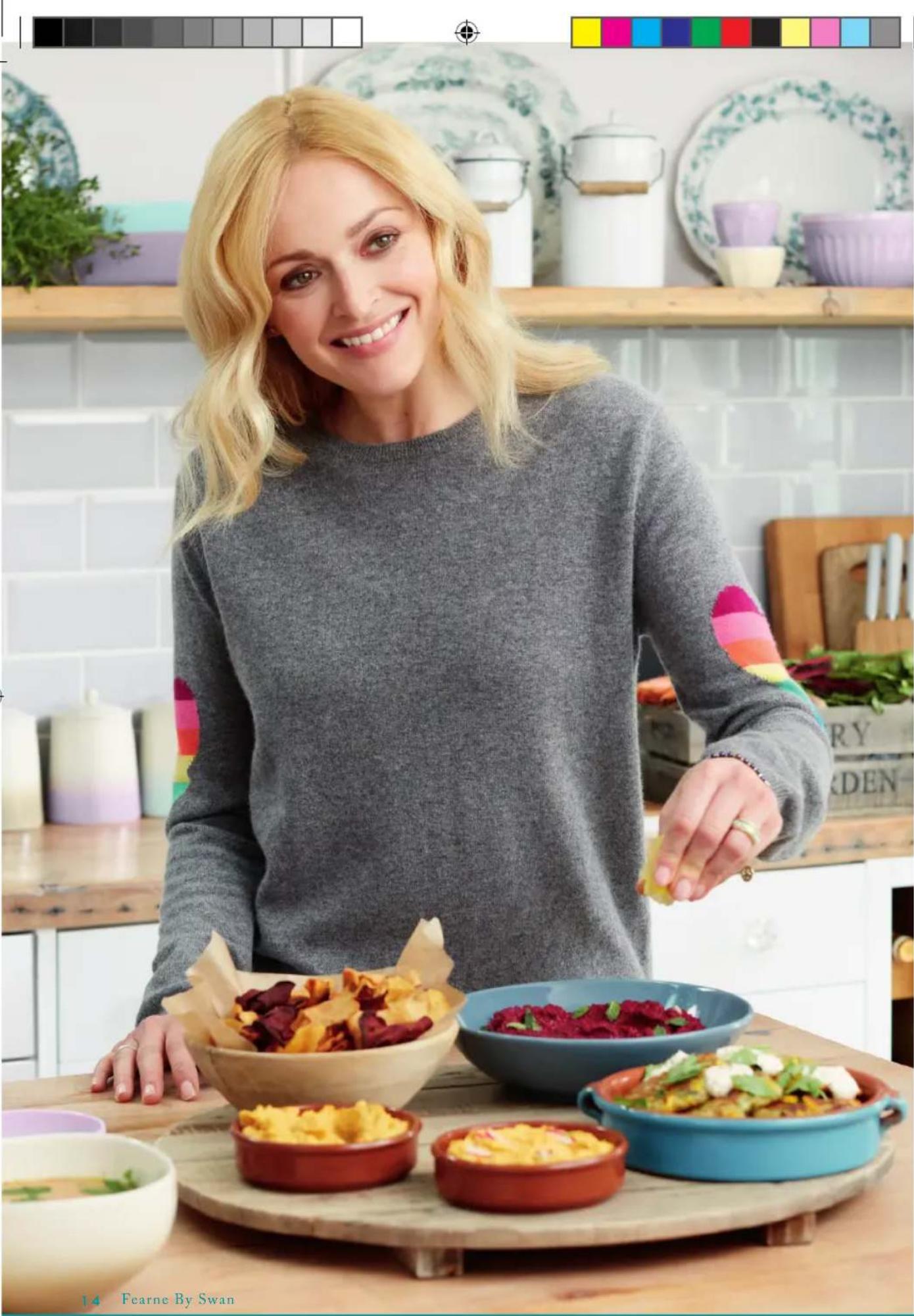 Woman smiling while holding a lemon in a kitchen, surrounded by colorful food bowls and decorative plates (no visible text or symbols)