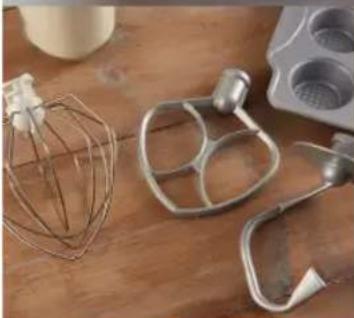 Close-up of kitchen utensils including a wire mixer, metal mixing bowl, and whisk on a wooden surface (no text or symbols visible)