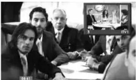 Black-and-white photo of a business meeting with visible name tags and a screen showing video content