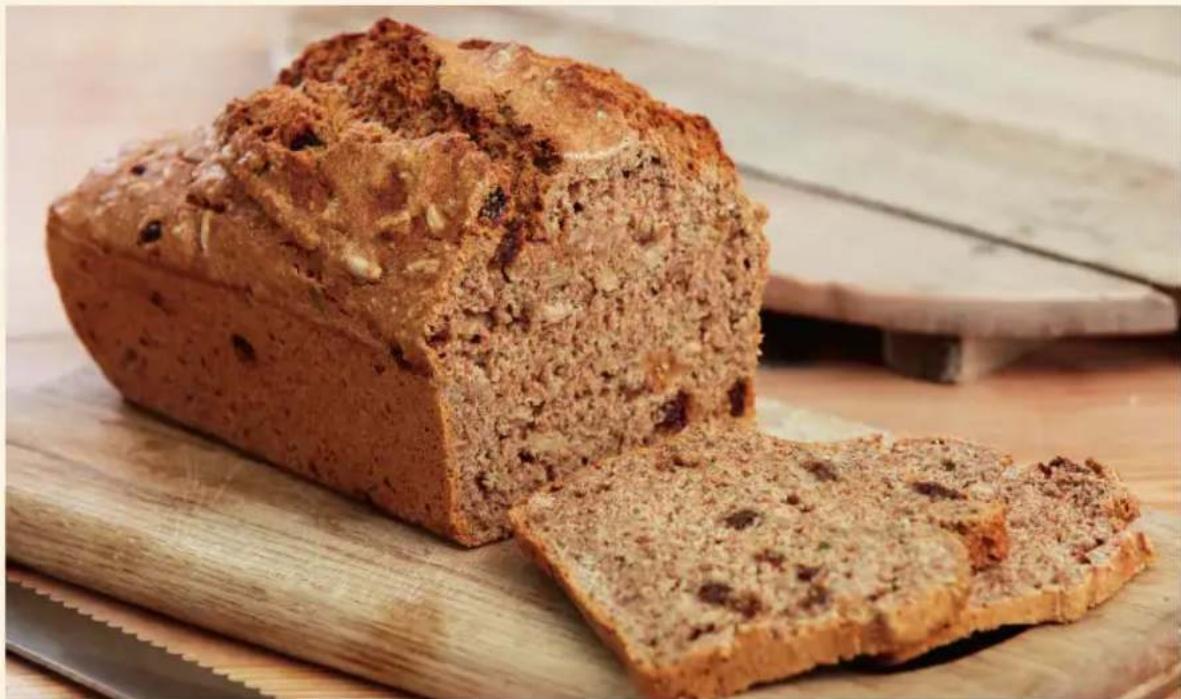 Close-up of a baked bread loaf on a wooden cutting board, showing sliced pieces and golden-brown crust (no text or symbols visible)