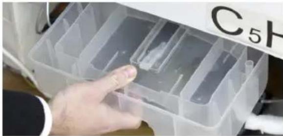 Close-up of a hand inserting plastic containers into a container labeled C5H (no text or symbols on the container itself)