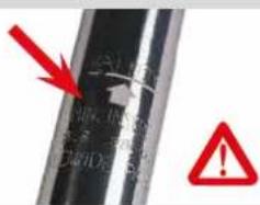 Close-up of a metallic cylindrical object with handwritten notes and red warning symbols