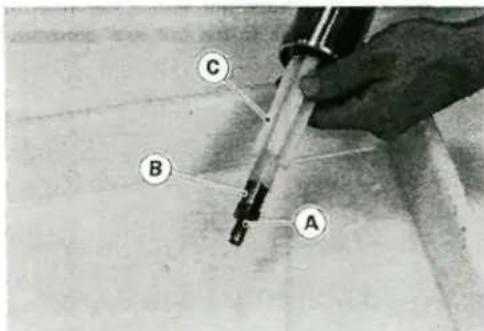 Close-up of a hand holding a soldering iron with labeled points A, B, and C on a surface