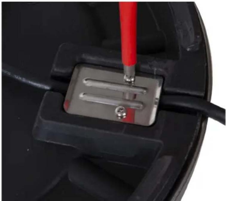 Close-up of a mechanical component with a red tool inserted, showing a metallic square base and wires (no text or symbols visible)