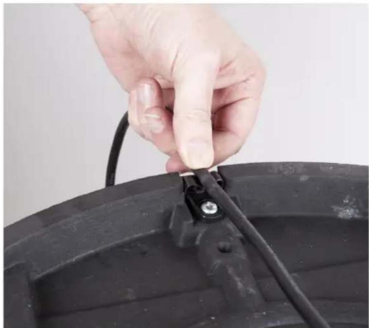 Close-up of a hand adjusting a black cable with a small connector, mounted on a dark plastic container (no text or symbols visible)