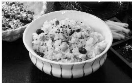 Black-and-white photo of a bowl of rice with sesame seeds, served on a patterned ceramic dish (no text or symbols visible)