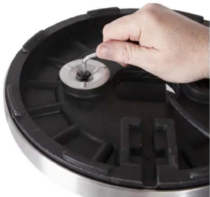 Close-up of a hand inserting a small metallic component into a black circular pot (no text or symbols visible)