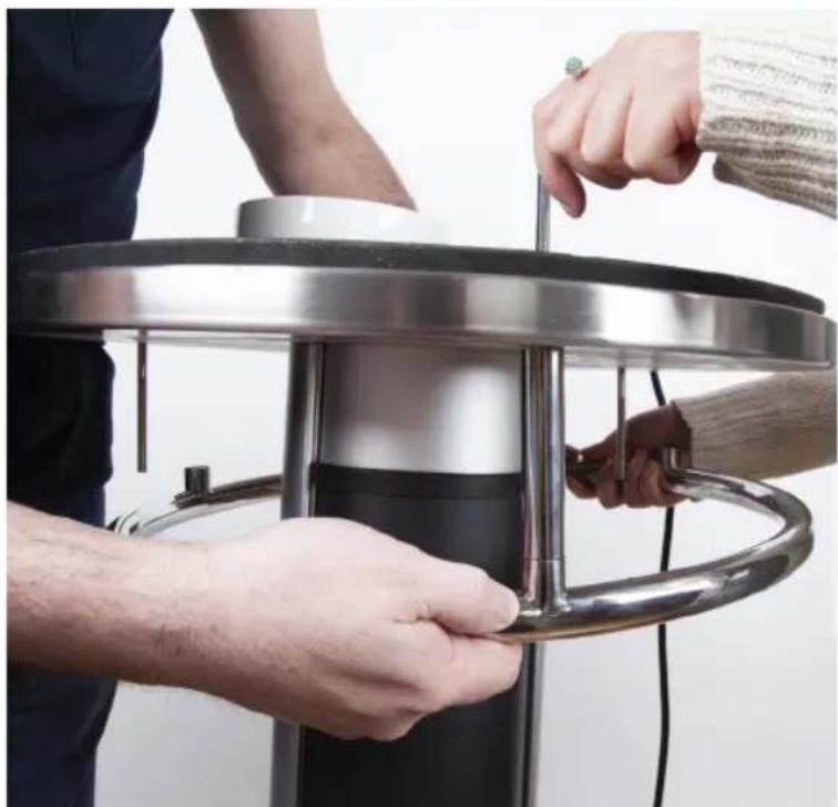 Close-up of hands operating a circular metal stand with a curved handle (no text or symbols visible)