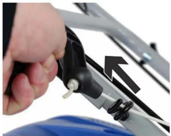Close-up of a hand holding a black cable clip attached to a metal frame, with an arrow pointing to the cable (no text or symbols visible)