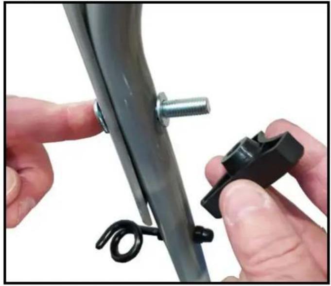 Close-up of hands adjusting a black plastic clip with a coiled spring attached to a metal bracket (no text or symbols visible)