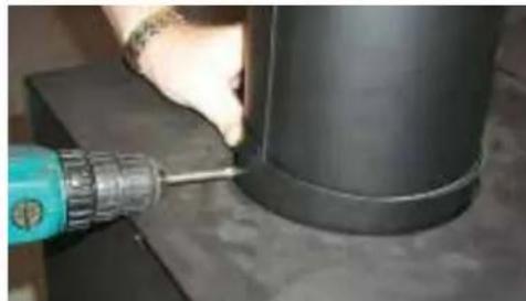 Close-up of a hand using a blue drill bit to apply material to a black cylindrical component (no visible text or symbols)