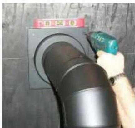 Person using a tool to clean or install a black pipe component on a wall (no visible text or symbols)