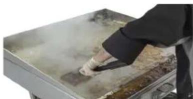 Person in chef uniform stirring food on a large griddle (no visible text or symbols)
