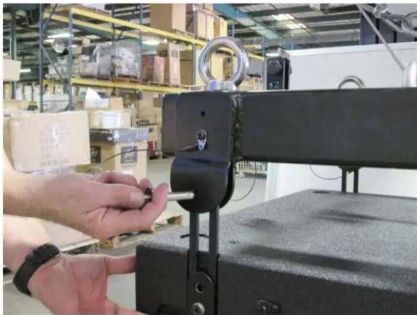 Person adjusting a black mechanical clamp in a warehouse with shelves of boxes in the background (no visible text or symbols)