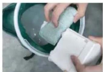 Person washing a green bowl with a white plastic container (no text or symbols visible)