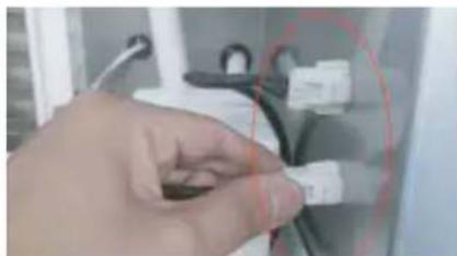 Close-up of a hand holding a small white connector, with a red circular overlay and black cable (no visible text or symbols)