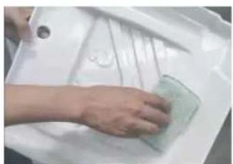 Hand cleaning a white plastic sheet with a green cloth (no text or symbols visible)
