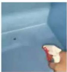 Close-up of a hand holding a red spray bottle against a blue tiled surface (no text or symbols visible)