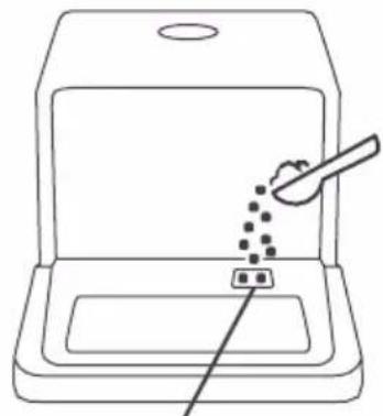 Line drawing of a kitchen appliance with a spoon and a small object inserted into the sink (no text or symbols).