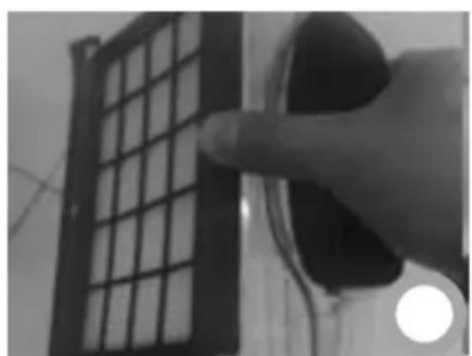 Close-up of a hand holding a black plastic object next to a grid-patterned panel (no visible text or symbols)
