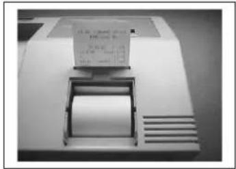 Scanned image of a printer or scanner with printed text and a paper, showing visible serial number and print details.