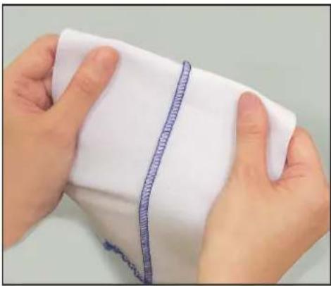 Close-up of hands holding a white fabric with a blue textured seam or seam, no visible text or symbols