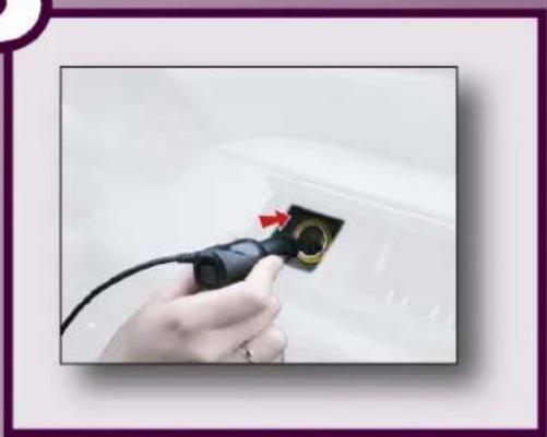 Hand holding a black plug inserted into a car, with a red arrow pointing to the plug (no text or symbols visible)