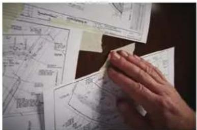 Hand holding a white paper with printed diagrams and annotations, likely illustrating technical drawings or calculations.
