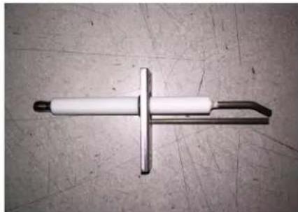 Close-up of a metallic tool with a cross-shaped handle and cylindrical body, resting on a textured surface (no text or symbols visible).