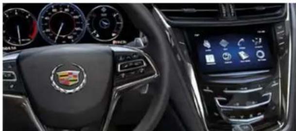 Interior view of a car dashboard with visible infotainment screens and a Cadillac logo (no readable text or symbols)