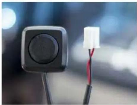 Close-up of a black square electronic device with a white connector and red wire, against a blurred blue background (no text or symbols visible)