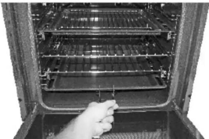 Interior view of an oven with a hand inserting a plug into the tray (no visible text or symbols)