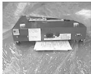 Black-and-white photo of an electronic device with visible printed labels and a paper sheet, likely from a technical or industrial document.