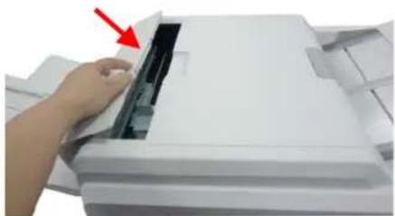 Close-up of a hand pressing down on a white paper printer cover with a red arrow pointing to the page (no text or symbols visible)