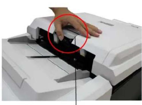 Close-up of a hand operating a white paper scanner with a black cover, showing a red circle highlighting the device (no text or symbols visible)