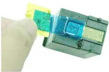 Hand holding a transparent electronic device with a green and blue component, no visible text or symbols