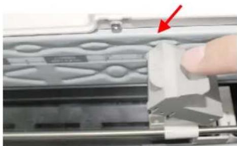 Close-up of a hand pressing a mechanical component on a textured surface, with a red arrow pointing to the component (no visible text or symbols)