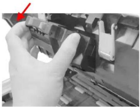 Close-up of a gloved hand holding a mechanical component, with a red arrow pointing to the part (no visible text or symbols)