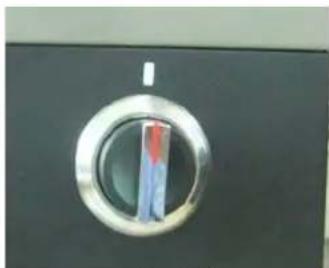 Close-up of a metallic circular button with a green and red stripe, mounted on a dark surface (no visible text or symbols)