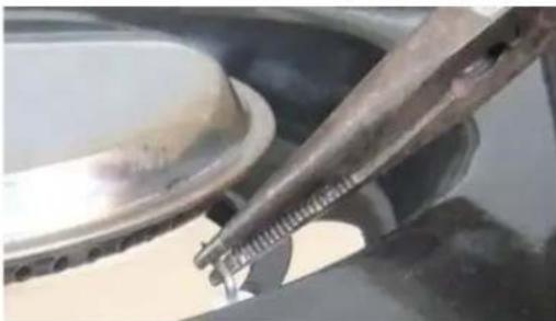 Close-up of a mechanical component with a metallic tool inserted, showing a threaded part and a circular component (no visible text or symbols)