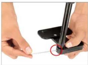 Close-up of hands using a tool to apply a small wire or cable to a black mechanical component (no text or symbols visible)