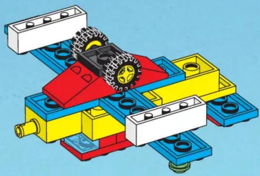 3D mechanical assembly diagram showing a red and yellow component with wheels and mounting brackets (no text or symbols)