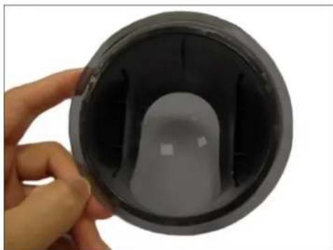 Hand holding a black circular object with internal structure, no visible text or symbols
