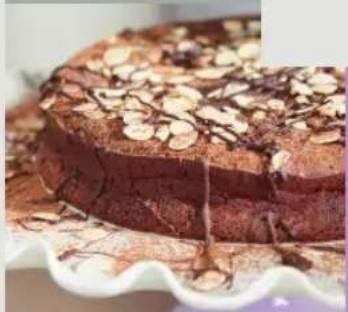 Close-up of a chocolate cake with nuts and chocolate drizzle on a white scalloped plate (no text or symbols visible)
